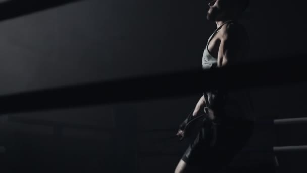 Male boxer wrapped in bandage jumping on the skipping rope in the dark ring. Slow motion. Silhouette. Boxing concept. — Stock Video