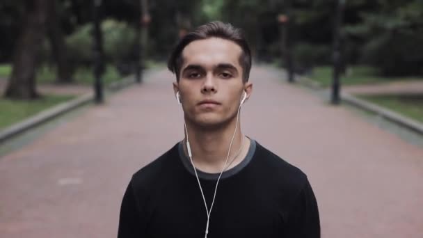 Retrato de joven atractivo en auriculares y Smartphone en su mano corriendo en el concepto del parque Vida saludable . — Vídeos de Stock