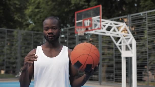 Fermer Portrait d'un jeune Afro musclé sérieux - Américain au chant blanc jouant avec le ballon, debout au Street Basketbal Court et regardant vers la caméra. Mode de vie sain et concept sportif . — Video