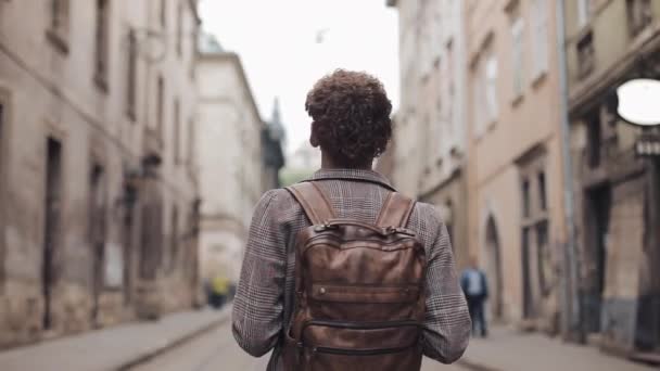 Vista posteriore del giovane turista con zaino marrone e auricolari che indossano giacca a quadri Passeggiando per la Old City Street, guardandosi intorno . — Video Stock