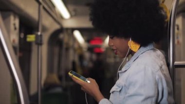 Müzik ve toplu taşıma cep telefonunda tarama dinlerken kulaklıklar genç Afrikalı Amerikalı kadınların portresi. Şehir ışıkları arka plan. Yavaş hareket.