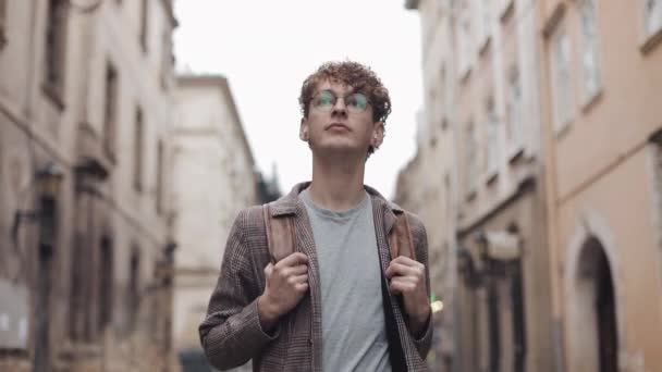 Ung Hipster Guy i glasögon bär incheckad jacka i hörlurar med Bag Walking, titta runt på Old City Street. Studerande, turistkonceptet. Resor. — Stockvideo