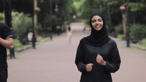 Junge Preety Musselin Mädchen trägt einen Hijabt im Park Treffen atrattraktive junge Mann läuft lächelnd Konzept gesunden Lebensstil. — Stockvideo