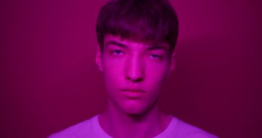 Beyaz tişörtlü genç adamın portresi. Doğrudan kameraya bakıyor. Fütürist Neon Pembe Işıklar 'da duruyor. Yaşam Tarzı ve İnsanlar Konsepti.