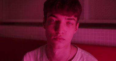 Beyaz tişörtlü genç adamın portresi. Doğrudan kameraya bakıyor. Fütürist Neon Pembe Işıklar 'da duruyor. Yaşam Tarzı ve İnsanlar Konsepti. Görüntüyü Kapat.