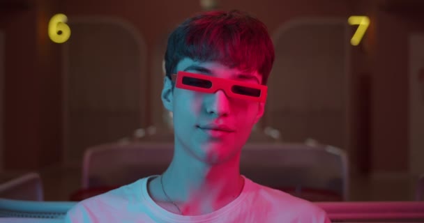 Beyaz tişörtlü, şık gözlüklü, Fütürist Neon Işıklandırma Numaraları Arkaplanda Doğrudan Kameraya Bakan Havalı Genç Adamın Kapanışı. Portre çekimi. — Stok video