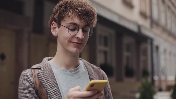 Giovani capelli ricci rossi Millennial in bicchieri, chat e sms su Smartphone utilizzando l'app di messaggistica, scorrendo sul suo schermo del cellulare. Rimane connesso e aggiornato . — Video Stock