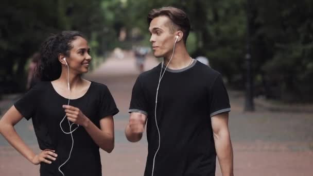 Jonge blanke man en Muslin meisje praten glimlachen en het opstijgen van koptelefoon op zoek gelukkig wandelen in het park mensen concept. — Stockvideo