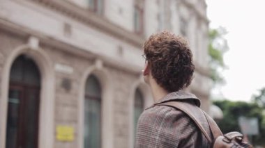 Gözlüklü Genç Millennial, Kulaklıklı ve İşaretli Ceket ve Kot Giyiyor, Çanta Yürüyor, Eski Şehir Caddesine Bakınıyor. Öğrenci, Turist Konsepti. Seyahat.