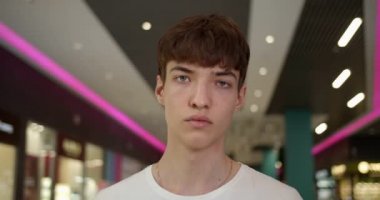 Mavi Gözlü Genç Adam 'ın portresi. Beyaz tişörtlü. Büyük Umut Merkezi' ndeki Neon Lights 'ta kameraya bakıyor. Görüntüyü Kapat.
