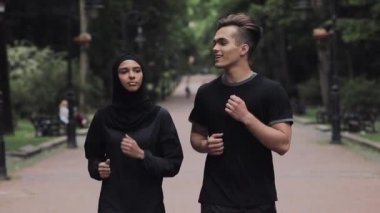 Genç beyaz adam ve Muslin kadın tesettürlü Parkta koşan heyecanlı ve rahat gülümseyen ve sohbet eden.