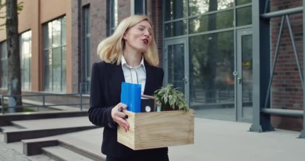 Vreugdevolle vrouw in de 30 voelt zich gelukkig terwijl ze ontslagen wordt en haar spullen draagt. Opgewonden vrouwelijke werknemer dansen en zingen tijdens het lopen en kijken in box op straat. Begrip werk. — Stockvideo