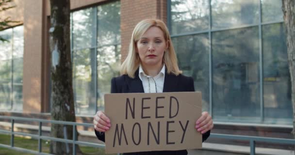 Frustrerad affärskvinna i 30-årsåldern får sparken och visar kartong banner med behöver pengar skriva. Kvinnlig arbetare förlorade jobbet och stod på gatan. Begreppet finanskris och arbetslöshet. — Stockvideo