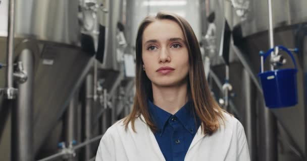 Vista da vicino donna concentrata in camice bianco camminando e guardando da parte. Ingegnere di processo femminile che controlla il lavoro delle apparecchiature automatiche per bevande. Concetto di birrificio e fabbrica di birra . — Video Stock