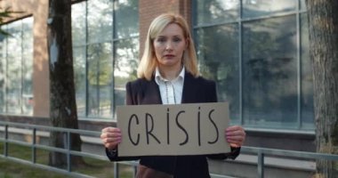 30 'lu yaşlarda işsiz bir kadın işçi sokakta dikilip kameraya bakıyor. Takım elbiseli mutsuz kadın, elinde karton pankartla iş bölgesinde kriz yazıları yazıyor. İşsizlik kavramı.