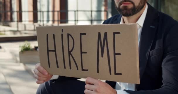 Vista de la cosecha de empleado masculino en busca de trabajo mientras está sentado en las escaleras en street.Dismissed hombre mostrando cartón con contratarme escribiendo en el distrito de negocios. Concepto de desempleo . — Vídeos de Stock