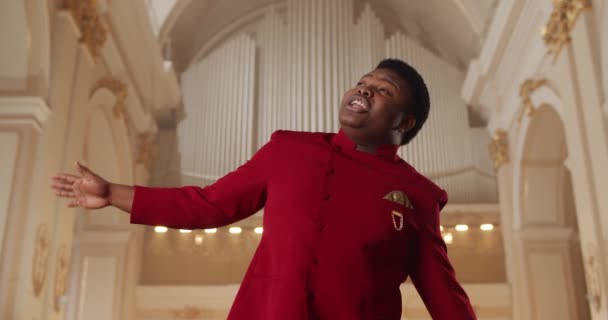 Veselý africký zpěvák evangelické hudby vystupující v modlitebně. Mladý muž v červeném obleku citově zpívá a pohybuje se v rytmu hudby. Koncept lidí a náboženství. — Stock video