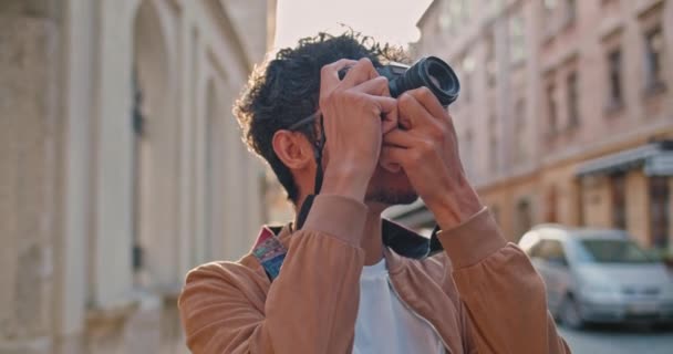 Vista de la cosecha de un joven con un anillo en la nariz tomando fotos del paisaje de la ciudad. Guapo turista masculino en gafas de pie en la vieja calle de la ciudad. Concepto de viaje, turismo y fotografía . — Vídeos de Stock