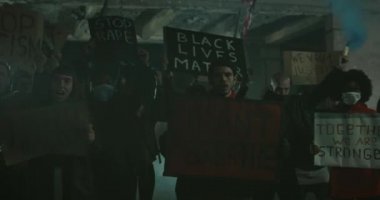 İnsanlar slogan atıp pankart tutarken polis şiddetini ve gece memurların ölümcül güç kullanımını protesto ediyorlar. Milenyum adamı pankart tutuyor ve kameraya bakıyor..
