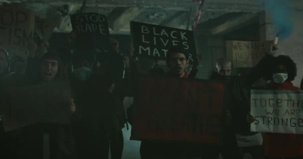 Pessoas cantando slogans e segurando banners enquanto protestam contra a brutalidade policial e o uso fatal da força por policiais à noite.Millennial cara segurando cartaz e olhando para a câmera . — Vídeo de Stock