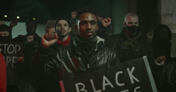混合民族の抗議者の群衆は、それらに書かれたスローガンでカートンのプラカードを保持しながら凍結し、握り拳を上げる。警察の残虐行為や人種差別に対するデモ. — ストック動画