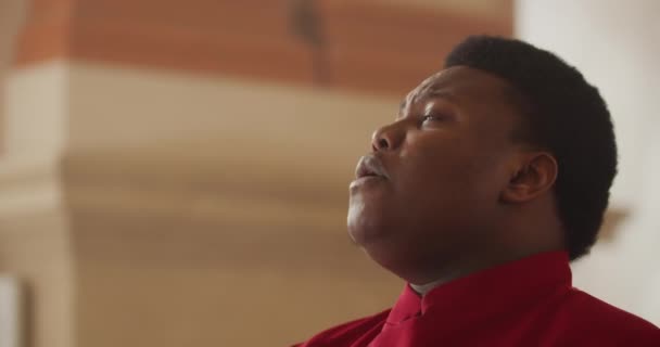 Side view of male performer wearing in red stylish suit singing emotionally. Portrait of afro american man performing worship music in church. Concept of religion. Blurred background. — Stock Video