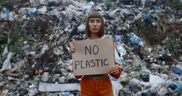 Ung seriös kvinna med näsa ring hålla kartong affisch med ingen plast skrift när du står framför skräp kulle. Flicka protesterar mot föroreningar.Begreppet ekologi skydd. — Stockvideo