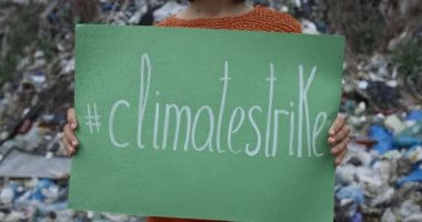 İklim grevinin yazılı olduğu grev tabelasını kaldıran kadın manzarası. Çöp tepesinin önünde dikilirken toprak kirliliğini protesto eden bir kadın. Ekolojik farkındalık kavramı.
