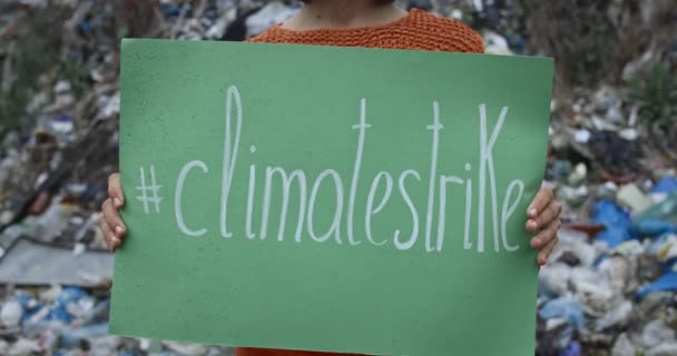 Vista de la cosecha de la persona femenina levantando señal de piquete con la escritura huelga climática. Mujer protestando contra la contaminación de la tierra mientras está de pie frente a la colina de basura. Concepto de conciencia ecológica . — Vídeos de Stock