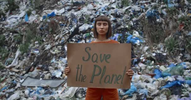 Ung flicka aktivist stödja rädda jorden rörelse. Millennial kvinna håller Save the Planet banner när du står framför skräp kulle. Ekologiskt skyddskoncept. Zooma in. — Stockvideo