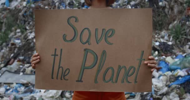 Vista de la cosecha de la persona femenina sosteniendo piquete signo con salvar el planeta escribiendo. Mujer protestando contra la contaminación de la tierra mientras está de pie frente a la colina de basura. Concepto de conciencia ecológica . — Vídeos de Stock