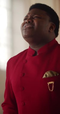 Kırmızı takım elbiseli Afro-Amerikan gospel şarkıcısına yakından bakın. Genç adam duygusal olarak ibadet müziği yapıyor ve vücudunu hareket ettiriyor..