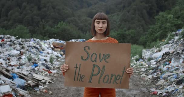 Mulher ativista segurando slogan agitação Salvar planeta. Rapariga lutando contra a poluição ecológica enquanto está em pé na floresta perto hil lixo. Aproxima. Conceito de protecção do ambiente . — Vídeo de Stock