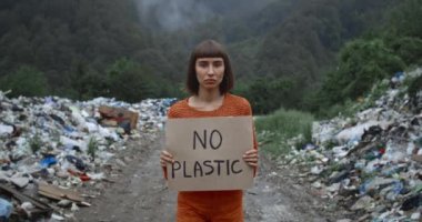 Ormanda çöp haplarının yanında plastik posteri olmayan kadın eylemci görüntüsü. Burun halkalı bir kız ekoloji grevini destekliyor. Çevre kirliliği kavramı.