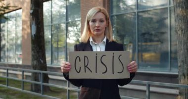 30 'lu yaşlarda sokakta kameraya bakan kadın çalışanı işten çıkarmışlar. Hüsrana uğramış bir kadın iş bölgesinde karton pankart ve kriz yazısı gösteriyor. İşsizlik kavramı.