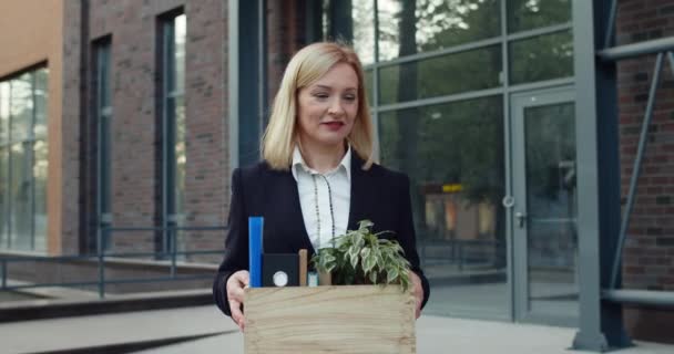 Happy woman in formal suit enjoy being fired and smiling while carrying her stuff. Excited female worker in formal clothes walking and looking in box with her belongings and saying yes. — Stock Video
