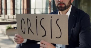 Ofis binasının yanında oturan erkek işçinin kriz pankartı gösterme görüntüsü. Takım elbiseli işsiz adam merdivenlerde eşyalarıyla birlikte oturuyor. İşten çıkarma kavramı.