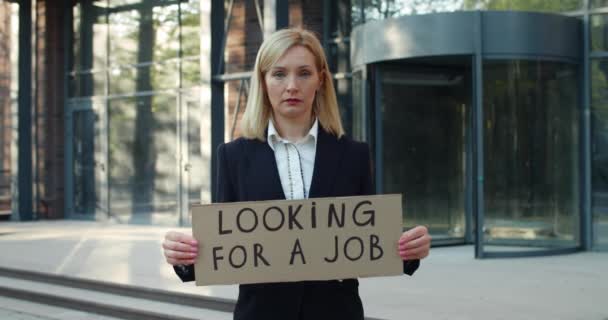 Dismissed female employee after pandemic lockdown. Woman in 30s wearing suit holding carton with with looking for job writing while standing at street and looking to camera. — Stock Video