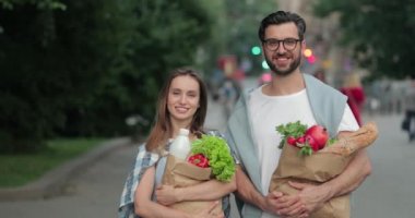 Birbirlerine bakıp gülümseyen güzel bir çiftin portresi. 30 'lu yaşlarda, elinde poşetlerle sokakta bekleyen neşeli bir adam ve kız..