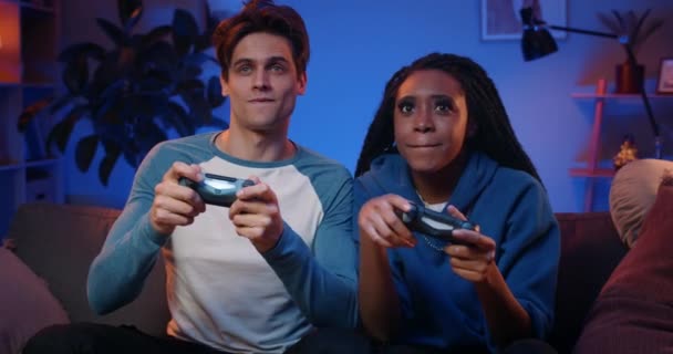 Feliz novio y novia jugando videojuegos y sosteniendo joysticks en casa. Millennial pareja disfrutando del juego mientras se sienta en el sofá y pasar tiempo libre. Concepto de relación. — Vídeos de Stock