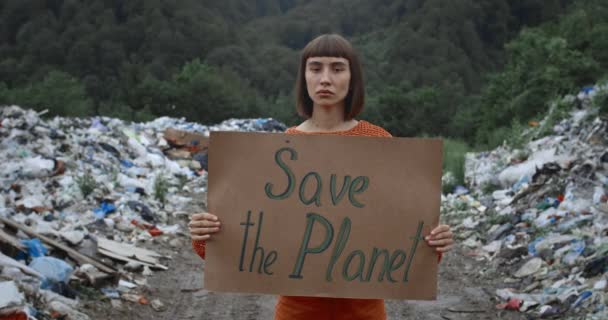 Női aktivista a Save the Planet ökológia poszterével.Nő támogatja a klíma sztrájk mozgalom, miközben közel áll a halom szemét az erdőben. Az ökológia koncepciója és az anyaföld megmentése. — Stock videók