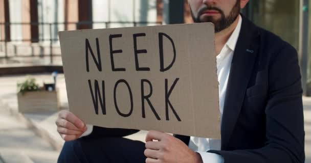 Crop view of male worker holding carton banner with need work writing. Man searching for job while sitting at street. Concept of financial global crisis and unemployment. — Stock Video