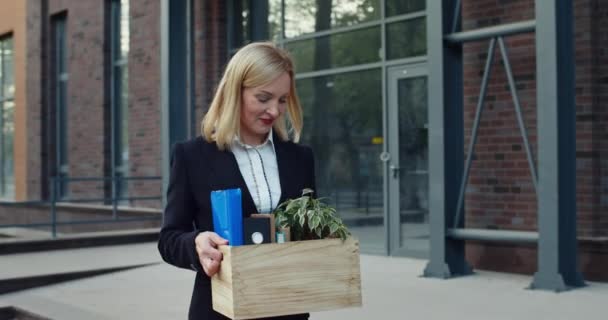Excited businesswoman in formal suit rejoicing while getting promotion and carrying her stuff. Happy woman smiling broadly while walking and looking in box with her belongings at street. — Stock Video