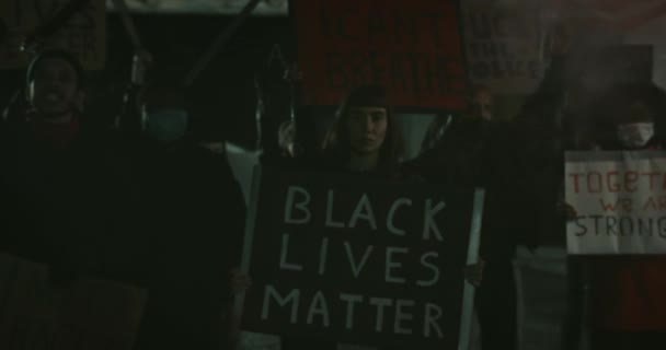 Fiatal női aktivista, aki fekete életű zászlót tart, miközben az utcán áll. Az emberek kiabálnak és szlogeneket tartanak, miközben lázadnak a rendőri brutalitás ellen. Közelíts rá!. — Stock videók