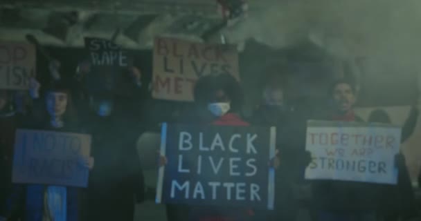 Afro american girl activist holding banner with black lives matters writing while standing in smoke at street. People shouting and holding slogans while rioting against police brutality. — Stock Video