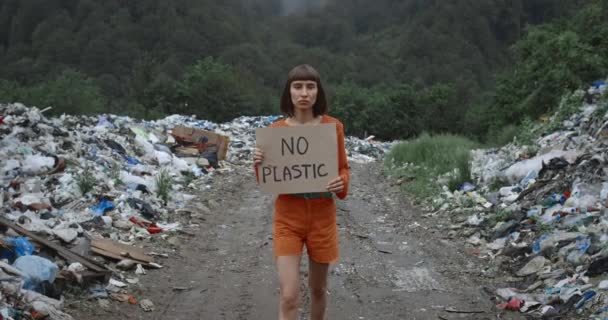 Chica seria sin cartel de plástico caminando cerca de pastillas de basura en el bosque. Mujer joven con anillo en la nariz apoyando el movimiento de huelga de ecología. Concepto de contaminación ambiental y salvar la Tierra . — Vídeos de Stock