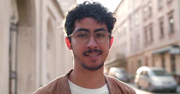 Vue rapprochée du jeune homme à lunettes regardant vers la caméra et souriant. Portrait de beau mec avec anneau de nez debout à la rue de la vieille ville.Concept de personnes et de la vie réelle. — Video