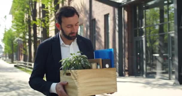 Homem bonito em terno formal que parece feliz e sorrindo ao obter novo emprego. Trabalhador masculino animado na década de 30 carregando e olhando para suas coisas enquanto caminhava perto do edifício moderno . — Vídeo de Stock