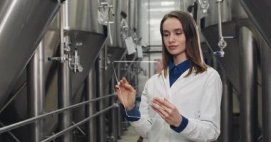 Verileri girerken ve sıra sıra demlenen fıçılarda dikilirken kadınların boş ekrana dokunmasını sağlayan ekin görüntüsü. Laboratuvar önlüklü bir bira fabrikası çalışanı, şeffaf cam tablet kullanıyor..