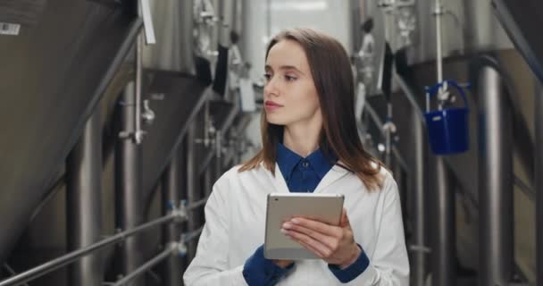 Un bell'ingegnere di processo donna che tiene registri su tablet al birrificio. Lavoratrice toccare e digitare display digitale mentre cammina e guardando su strumenti calibri. — Video Stock
